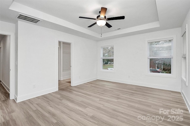 empty room with light wood-type flooring, plenty of natural light, visible vents, and a tray ceiling