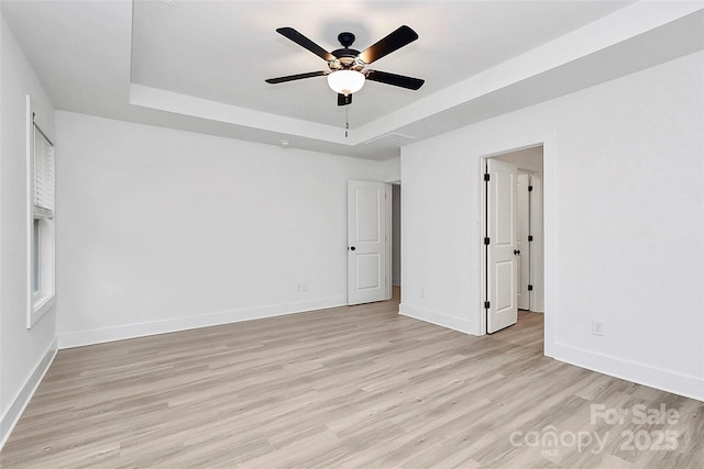 unfurnished bedroom featuring baseboards, a tray ceiling, and light wood-style floors