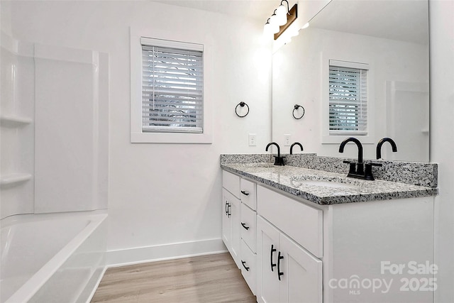 bathroom with wood finished floors, baseboards, a sink, and a healthy amount of sunlight