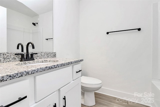 bathroom featuring toilet, baseboards, walk in shower, wood finished floors, and vanity
