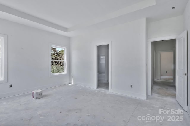 unfurnished bedroom featuring a raised ceiling, baseboards, and connected bathroom