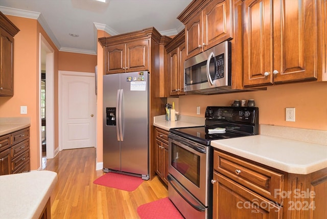 kitchen with appliances with stainless steel finishes, ornamental molding, and light hardwood / wood-style floors