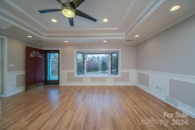 unfurnished living room with a raised ceiling, crown molding, light hardwood / wood-style flooring, and ceiling fan