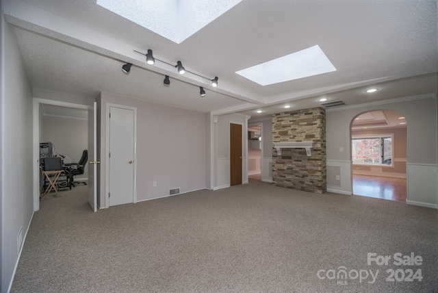 unfurnished living room featuring carpet flooring, a skylight, ornamental molding, a textured ceiling, and a stone fireplace