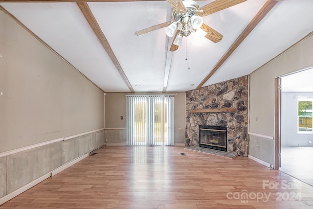 unfurnished living room with light wood-type flooring, ceiling fan, a stone fireplace, and vaulted ceiling with beams