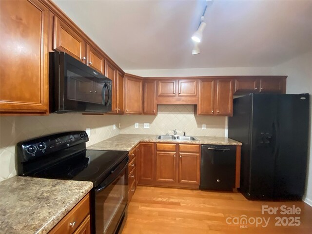 kitchen with black appliances, rail lighting, sink, light stone counters, and light hardwood / wood-style floors