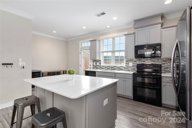 kitchen featuring gray cabinets, a kitchen island, sink, black appliances, and crown molding