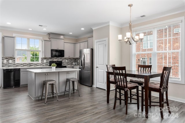 kitchen with a breakfast bar area, gray cabinetry, decorative light fixtures, a kitchen island, and black appliances