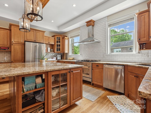 kitchen with high quality appliances, an inviting chandelier, wall chimney range hood, light hardwood / wood-style floors, and light stone counters