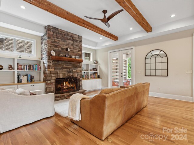 living room with ceiling fan, a fireplace, beamed ceiling, and light hardwood / wood-style flooring