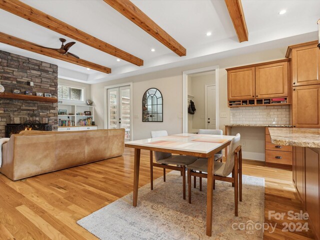 dining room with a fireplace, beam ceiling, light wood-type flooring, and ceiling fan