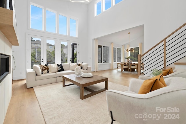 living room featuring a towering ceiling, french doors, a chandelier, and light hardwood / wood-style floors