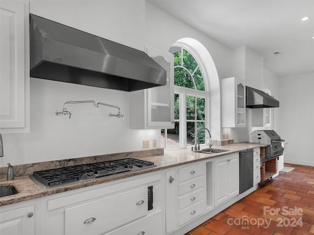 kitchen with stainless steel gas stovetop, sink, white cabinets, and wall chimney exhaust hood