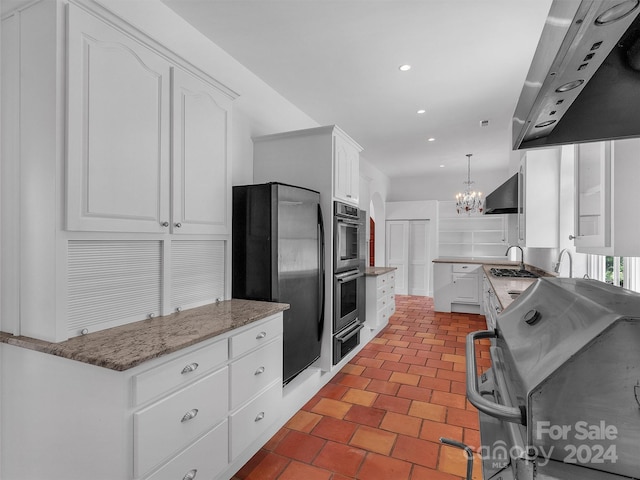 kitchen featuring wall chimney exhaust hood, light stone counters, decorative light fixtures, stainless steel appliances, and white cabinets