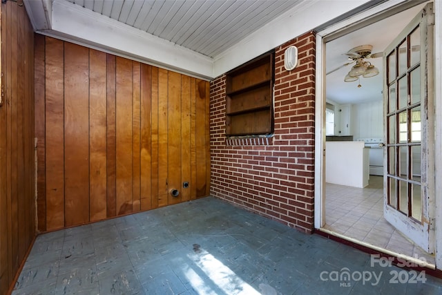 unfurnished room featuring ceiling fan, brick wall, and wood walls