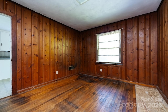 empty room with wood-type flooring, wooden walls, and baseboards