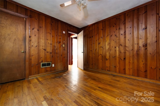 empty room featuring wooden walls, baseboards, visible vents, ceiling fan, and hardwood / wood-style floors