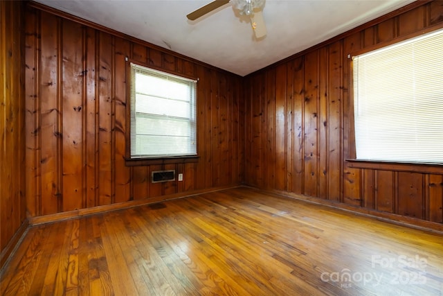 empty room with ceiling fan, hardwood / wood-style floors, wood walls, and a wealth of natural light