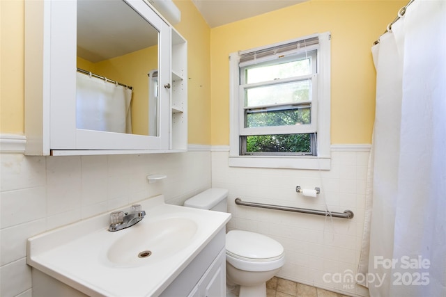 bathroom featuring toilet, wainscoting, tile walls, and vanity