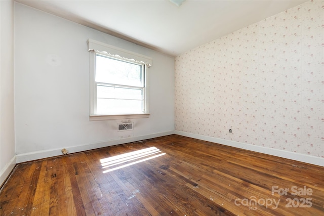 empty room with vaulted ceiling, wood-type flooring, baseboards, and wallpapered walls