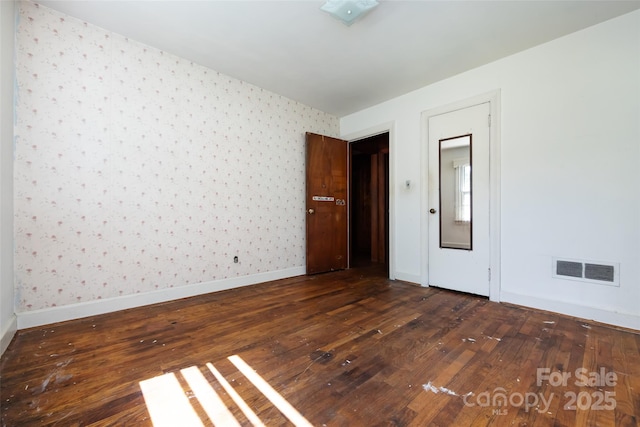 spare room with visible vents, dark wood finished floors, baseboards, and wallpapered walls