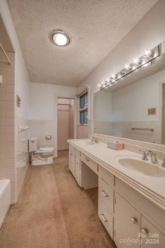 bathroom featuring a textured ceiling, vanity, toilet, and tile walls