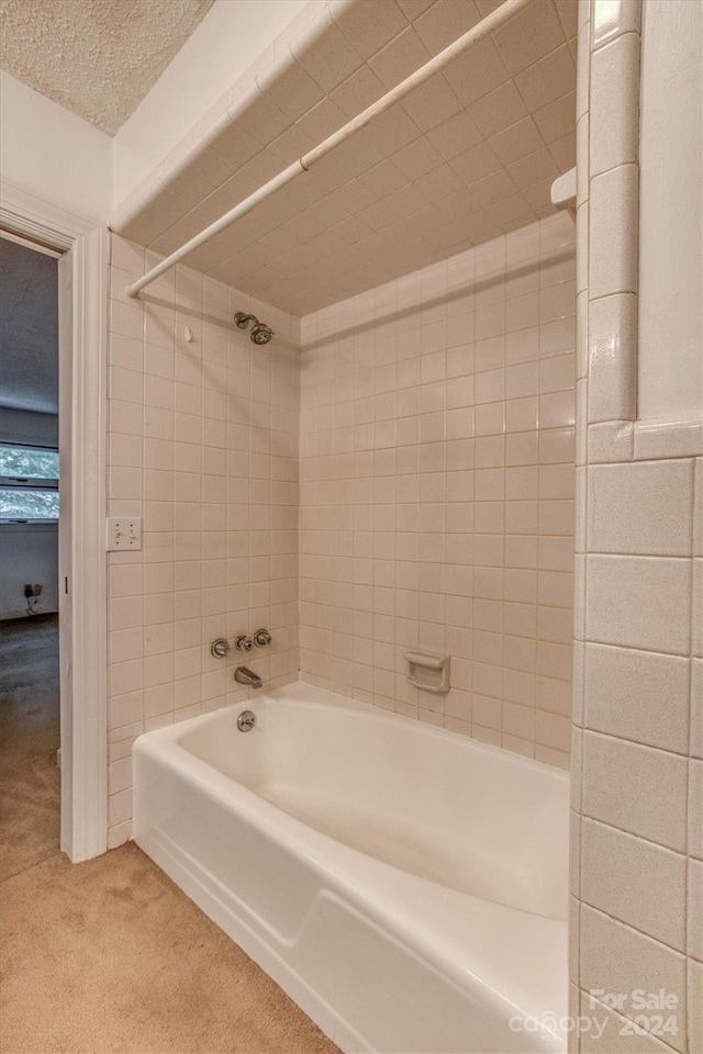 bathroom featuring a textured ceiling and tiled shower / bath