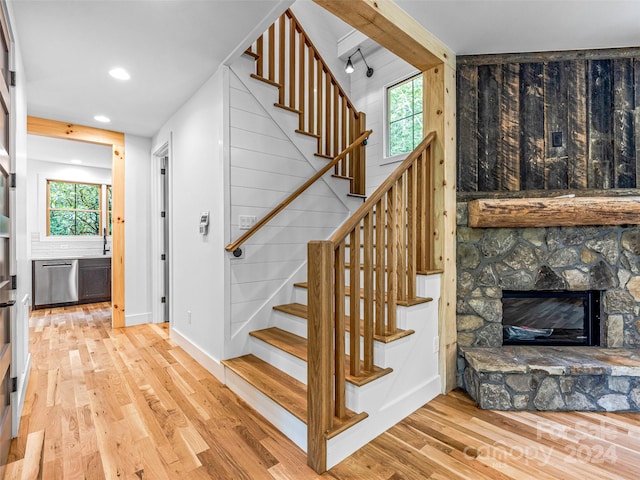 stairs with light hardwood / wood-style floors and a stone fireplace