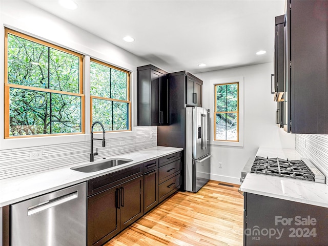 kitchen featuring appliances with stainless steel finishes, light hardwood / wood-style flooring, sink, light stone counters, and backsplash