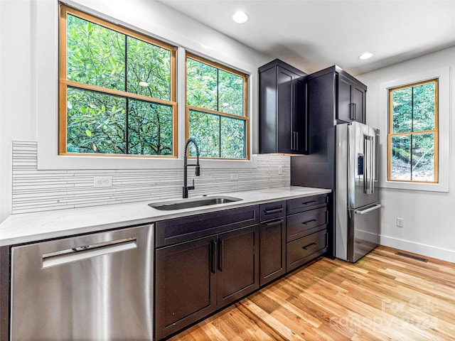 kitchen featuring appliances with stainless steel finishes, light hardwood / wood-style flooring, sink, backsplash, and light stone countertops