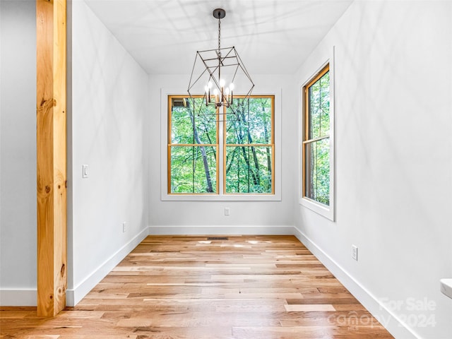 unfurnished room with a healthy amount of sunlight, light hardwood / wood-style flooring, and an inviting chandelier