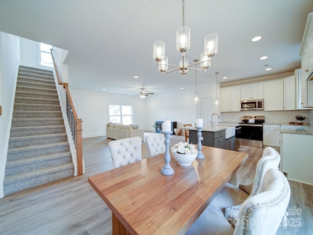 dining space featuring sink, ceiling fan with notable chandelier, and light hardwood / wood-style flooring