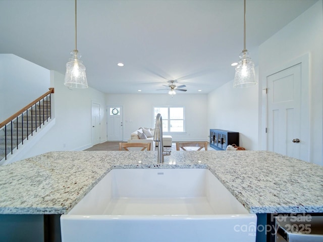 kitchen with an island with sink, sink, hanging light fixtures, light stone counters, and ceiling fan