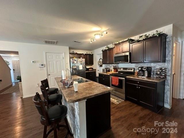 kitchen featuring a kitchen island with sink, dark wood-type flooring, sink, a kitchen bar, and stainless steel appliances