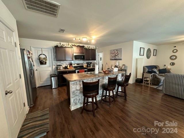 kitchen with appliances with stainless steel finishes, dark brown cabinets, a kitchen island with sink, sink, and a breakfast bar area