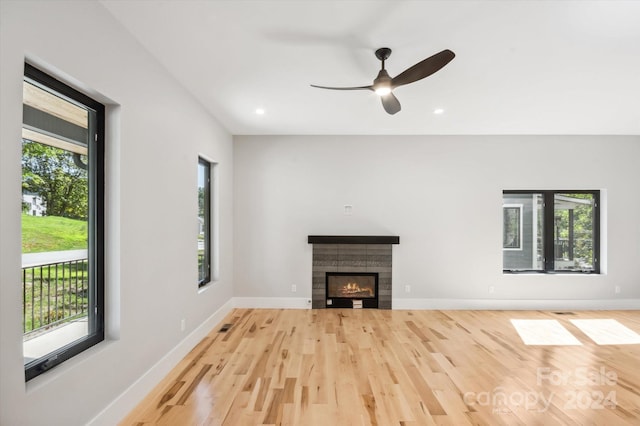 unfurnished living room featuring ceiling fan, a healthy amount of sunlight, a tiled fireplace, and light hardwood / wood-style floors