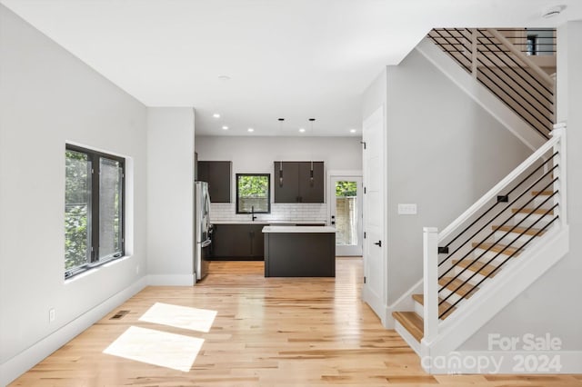 kitchen featuring a center island, decorative backsplash, stainless steel refrigerator, light hardwood / wood-style flooring, and dark brown cabinetry