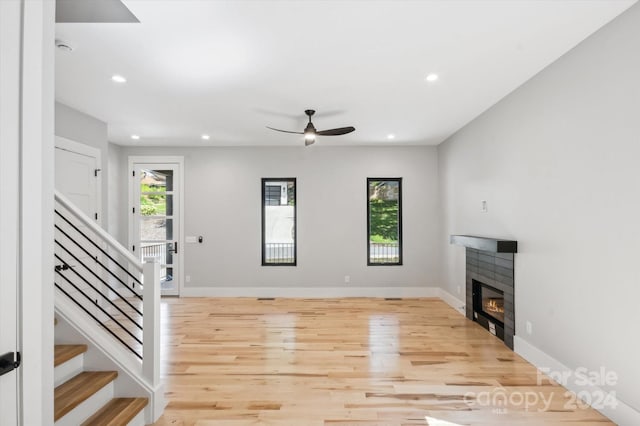 unfurnished living room featuring ceiling fan, plenty of natural light, a tile fireplace, and light hardwood / wood-style floors