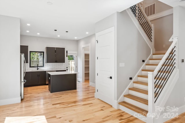 kitchen with pendant lighting, a kitchen island, decorative backsplash, sink, and stainless steel fridge