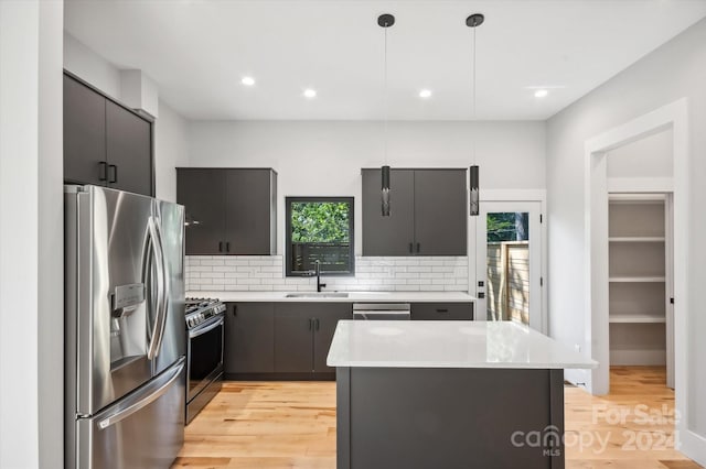 kitchen with appliances with stainless steel finishes, a center island, tasteful backsplash, decorative light fixtures, and sink