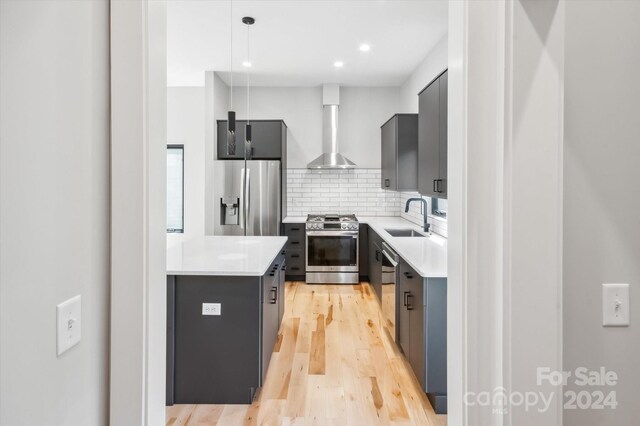 kitchen featuring appliances with stainless steel finishes, decorative backsplash, pendant lighting, wall chimney exhaust hood, and sink