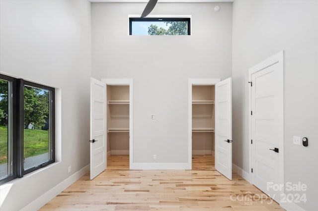 unfurnished bedroom featuring a high ceiling, two closets, and light wood-type flooring