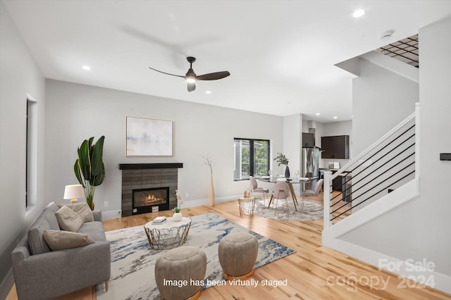 living room with ceiling fan, a tile fireplace, and light hardwood / wood-style flooring