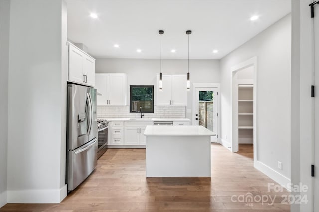 kitchen with pendant lighting, white cabinetry, stainless steel appliances, sink, and backsplash