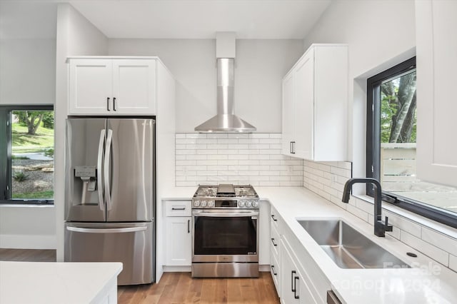 kitchen featuring appliances with stainless steel finishes, wall chimney range hood, white cabinetry, decorative backsplash, and sink