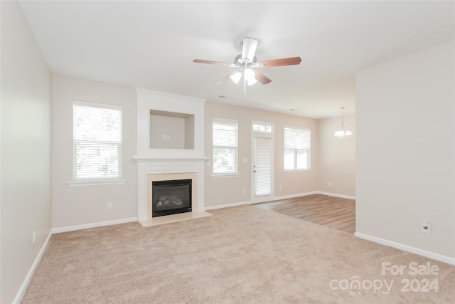 unfurnished living room featuring light carpet and ceiling fan with notable chandelier