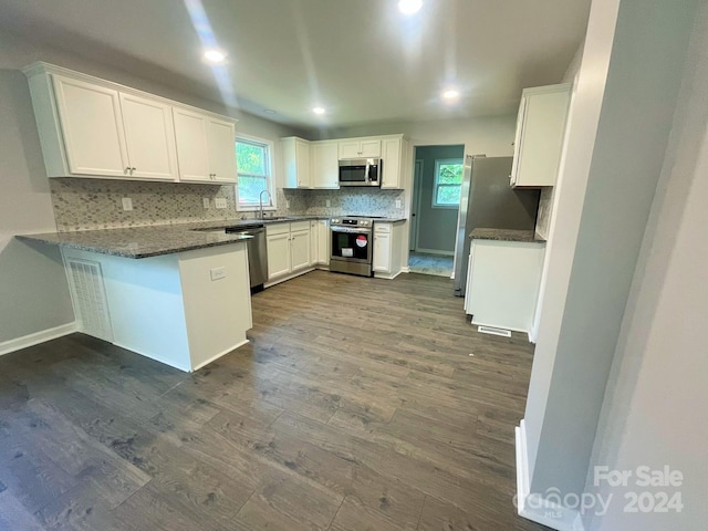 kitchen with kitchen peninsula, appliances with stainless steel finishes, dark hardwood / wood-style flooring, sink, and white cabinets