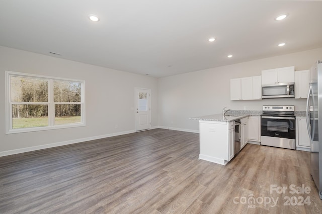 kitchen with light stone counters, appliances with stainless steel finishes, kitchen peninsula, light hardwood / wood-style floors, and white cabinets