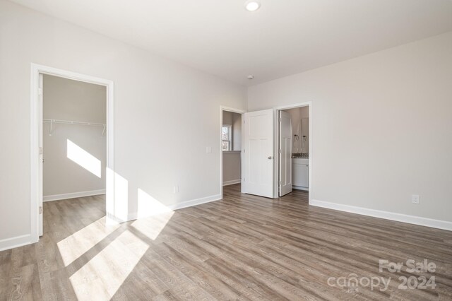 unfurnished bedroom featuring a walk in closet, connected bathroom, hardwood / wood-style floors, and a closet