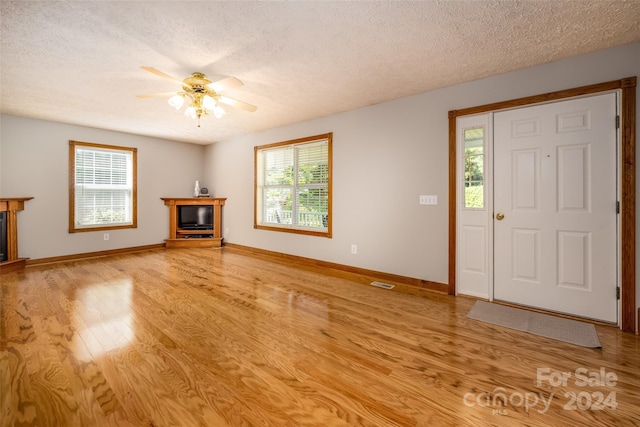 unfurnished living room with ceiling fan, light hardwood / wood-style flooring, and a textured ceiling